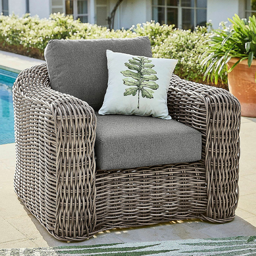 Grijze gevlochten tuinstoel met grijze kussens en decoratief kussen met bladmotief