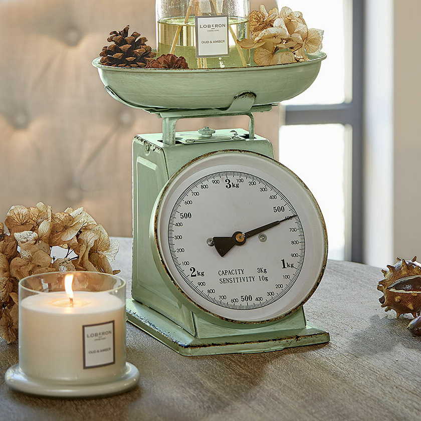 Mintgroene metalen keukenweegschaal met witte wijzerplaat en decoraties op houten tafel