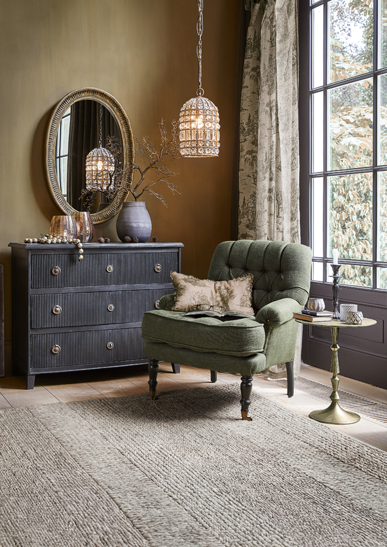Fauteuil vert confortable avec coussins près d'une commode noire et d'une table dorée dans un salon avec tapis