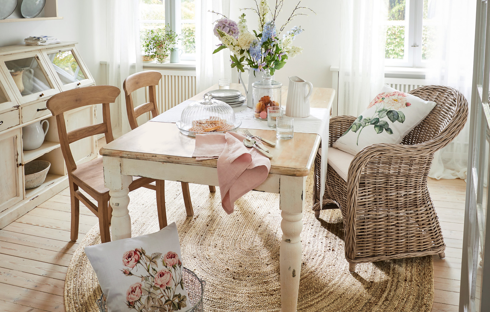 Shabby chic eetkamer met houten tafel, rotan stoel en bloemstuk in lichte ruimte