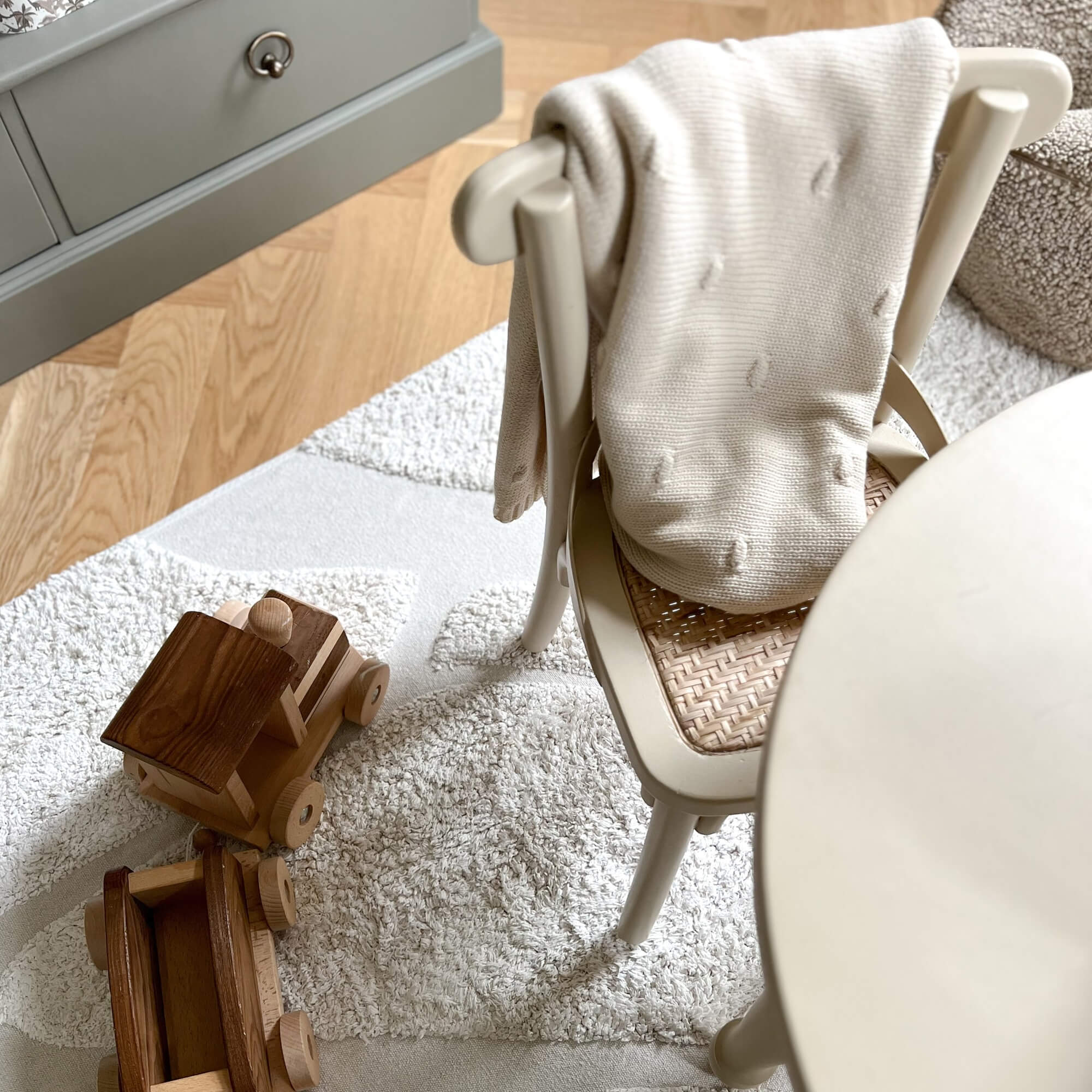 Beige gebreide deken op stoel met gevlochten zitting naast houten speelgoed op lichte vloerkleed