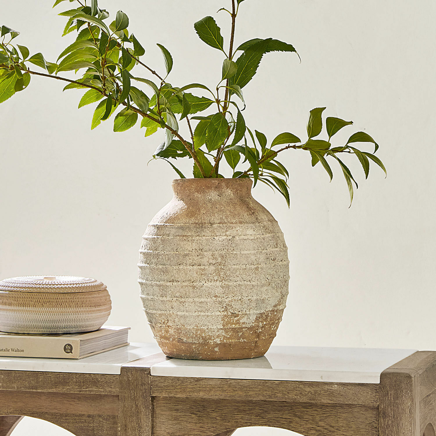 Rustieke keramische vaas in beige-bruin met groene takken op een houten tafel