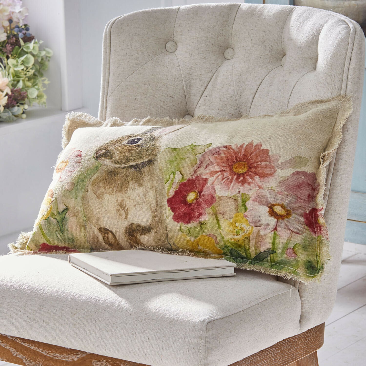 Housse de coussin Parélys Coussin rectangulaire en lin avec motif lapin et fleurs colorées sur fauteuil beige clair