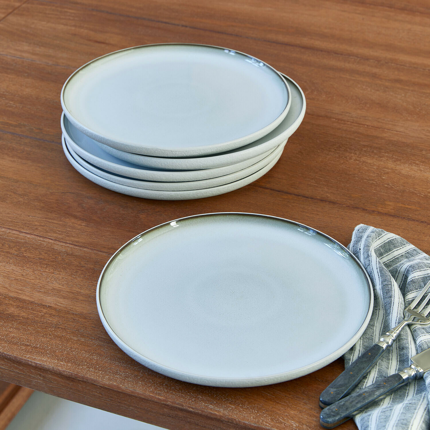 Bord set van 6 Eiruna Set lichtgrijze keramische borden met subtiele groene rand op houten tafel met bestek