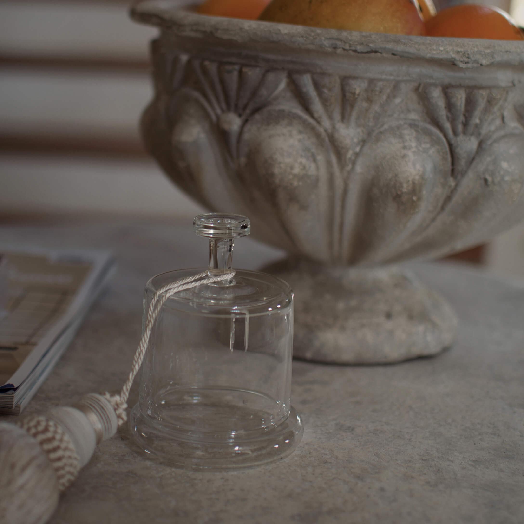 Cloche décorative en verre transparent avec corde blanche posée sur une table en pierre à côté d'une coupe ornée