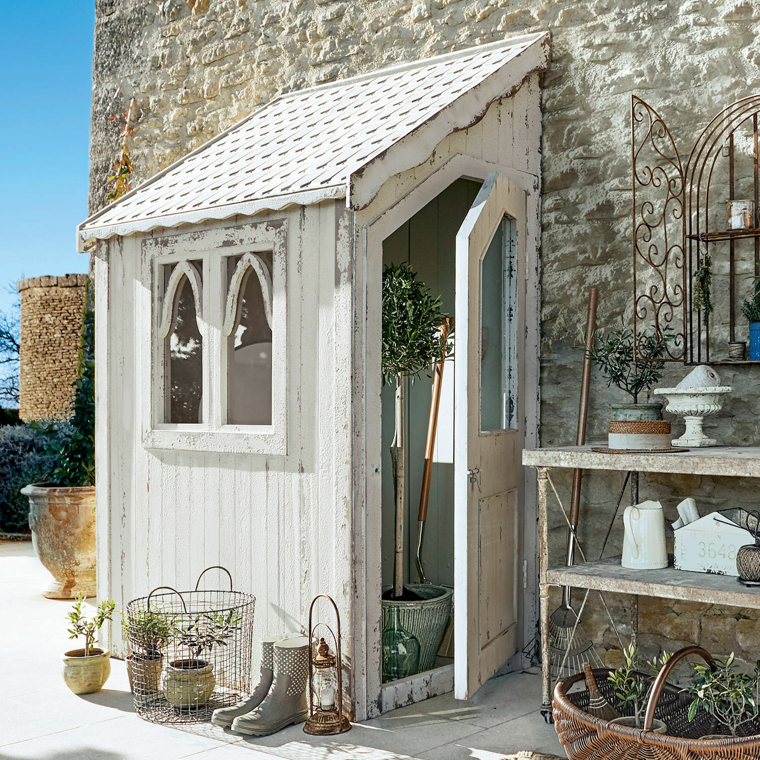 Tuinhuis Lettret Witte houten tuinhuisje met ramen en open deur, planten en decoratieve tuingereedschappen