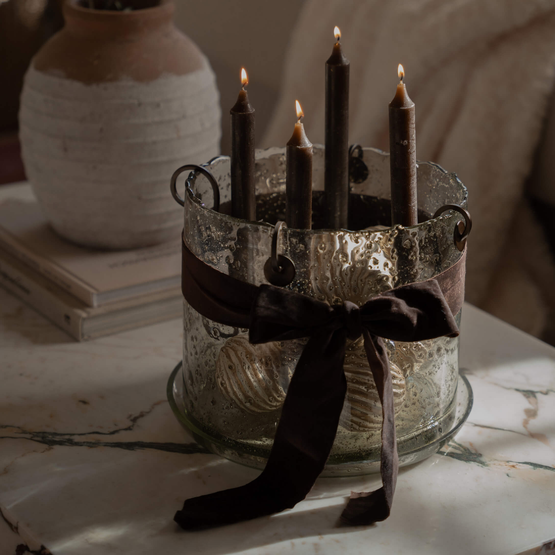 Bougeoir en verre avec quatre bougies noires et un ruban marron sur une table en marbre