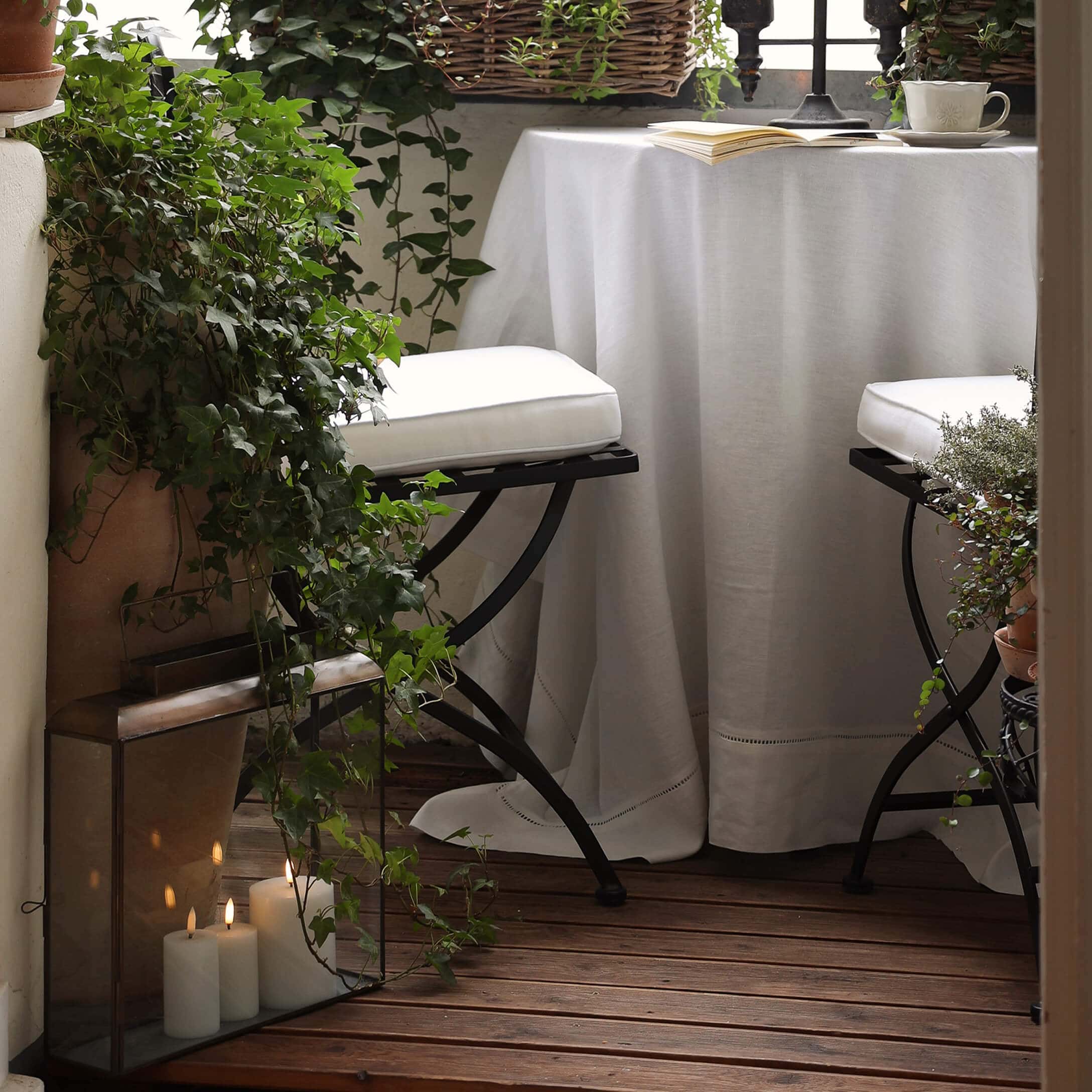 Balcon chaleureux avec plancher en bois, nappe blanche et chaises en métal avec coussins blancs