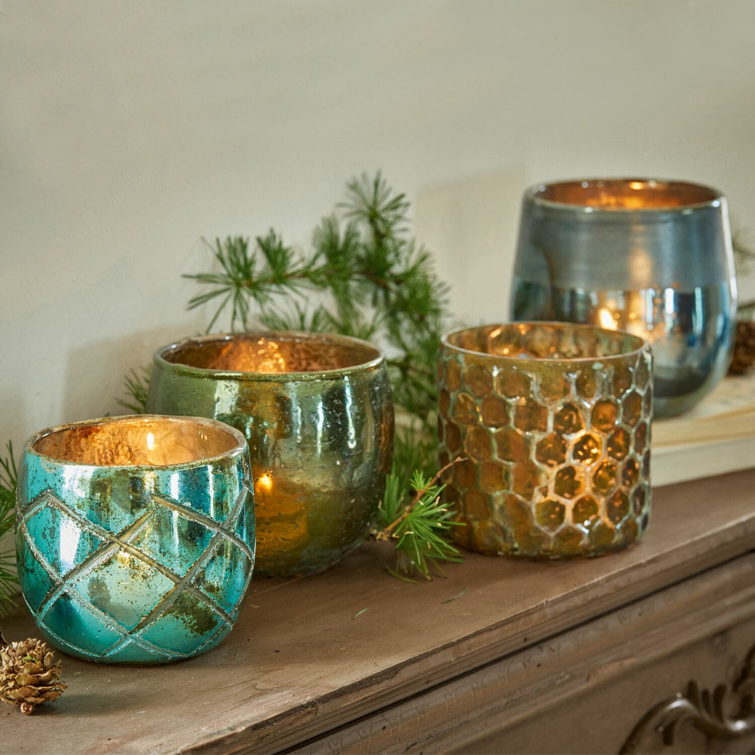 Set van vier glazen theelichthouders in turquoise, groen en goud op een houten plank