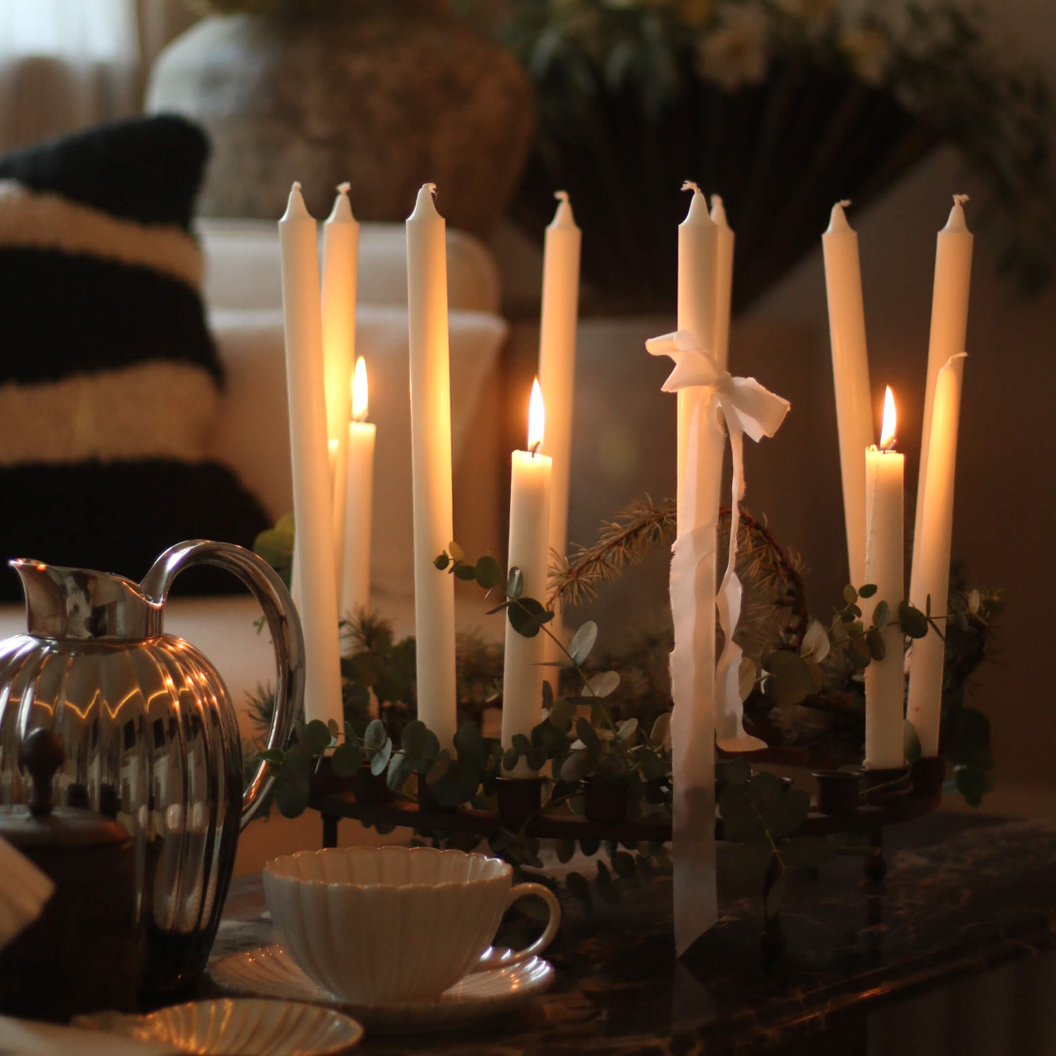 Chandelier décoratif avec bougies blanches et feuillage vert sur une table dans un intérieur chaleureux