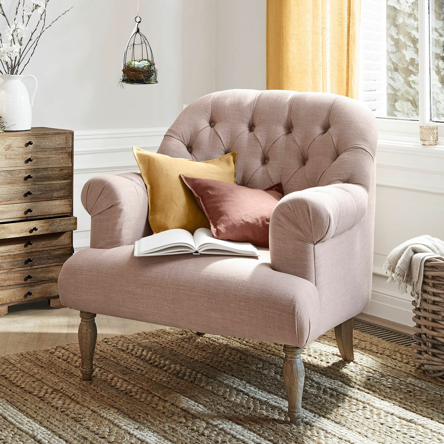 Fauteuil Shambrook Roze gestoffeerde bank met houten poten en twee warme gekleurde kussens op een natuurlijke geweven vloerkleed