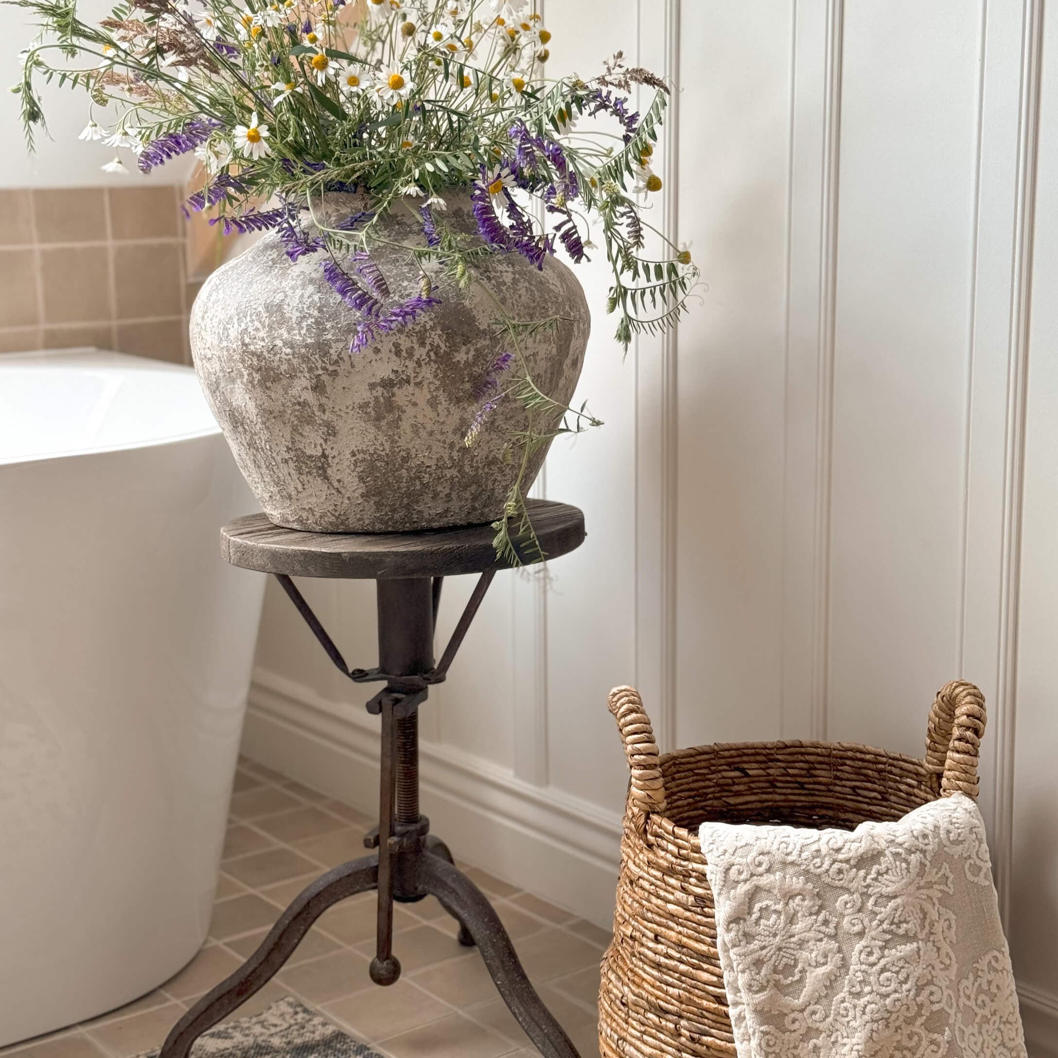 Vase rustique en pierre grise avec fleurs des champs sur un support en métal dans une salle de bain