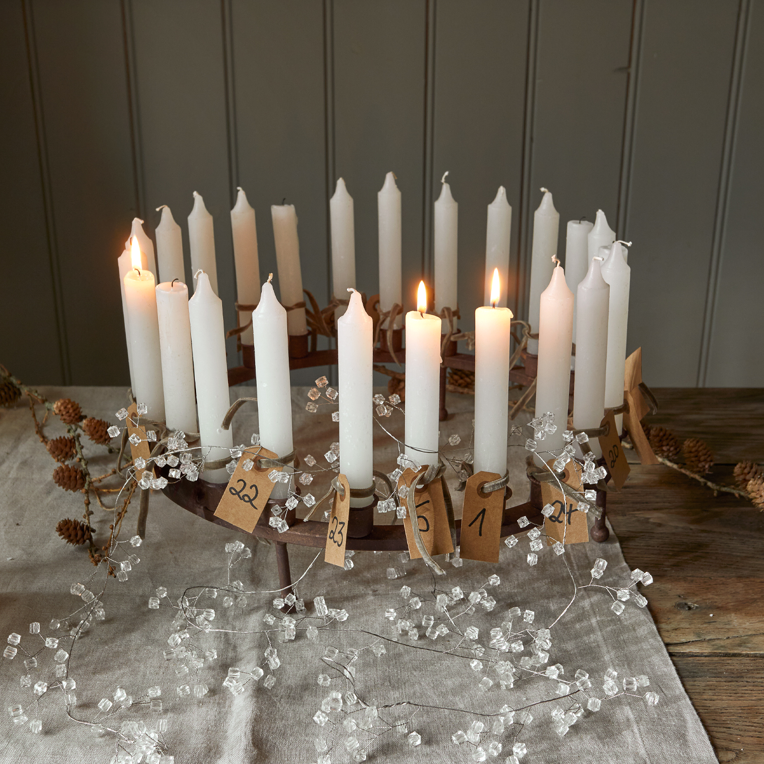 Couronne de l'Avent en métal avec 24 bougies blanches numérotées sur une nappe en lin et décorations transparentes