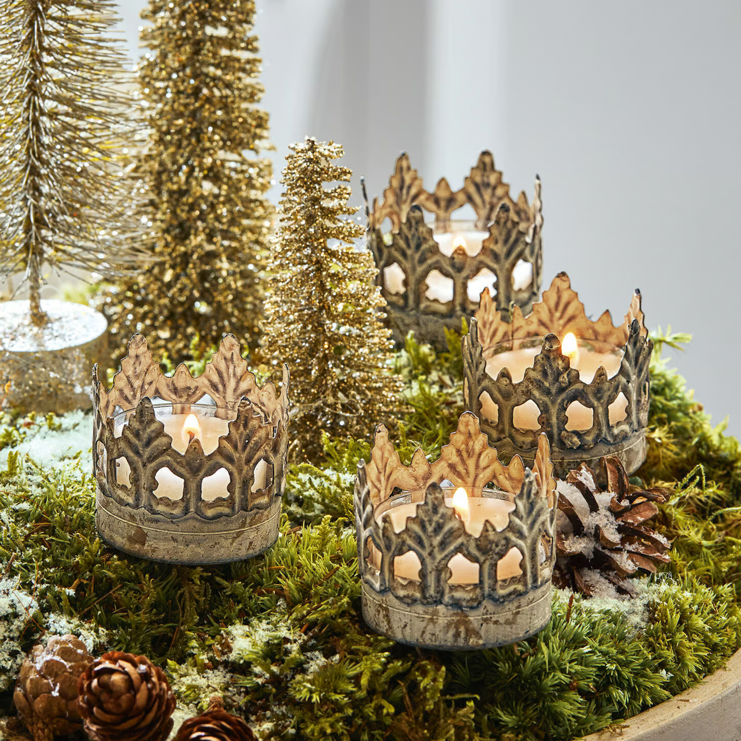 Photophores en métal en forme de couronne sur mousse verte avec décorations de Noël et sapins dorés