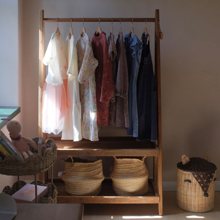 Penderie en bois avec robes pastel suspendues et paniers en osier dans une chambre d'enfant lumineuse