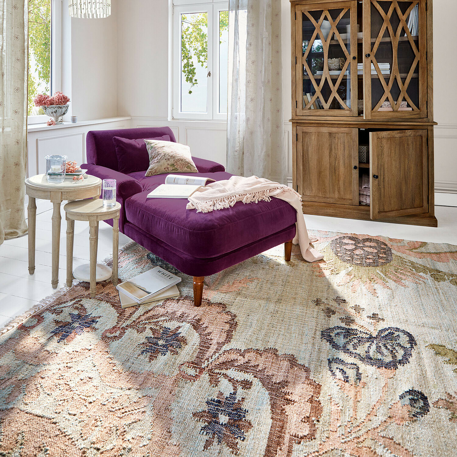 Vloerkleed Amélorie Paars fluwelen ligstoel in lichte woonkamer met houten vitrinekast en decoratief vloerkleed