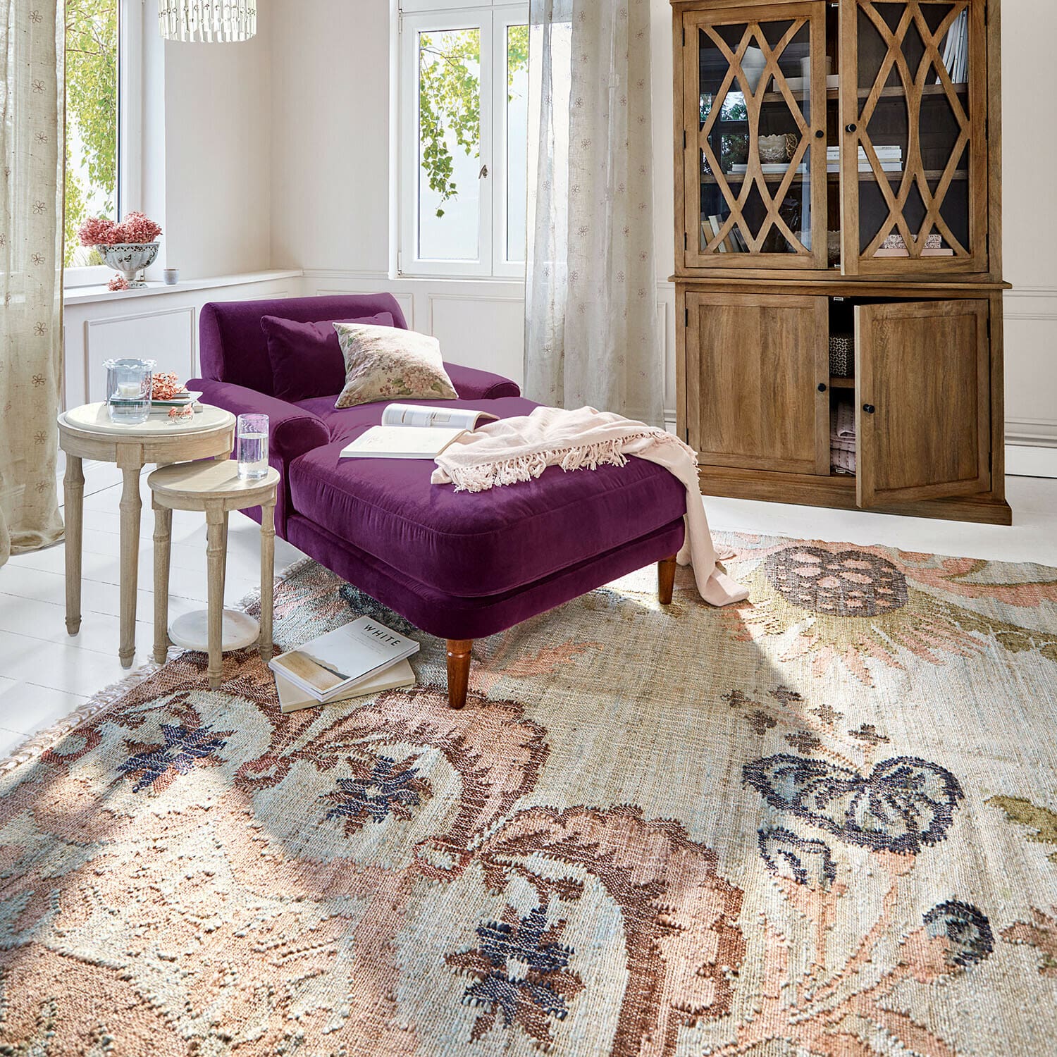 Vloerkleed Amélorie Paars fluwelen ligstoel in lichte woonkamer met houten vitrinekast en decoratief vloerkleed