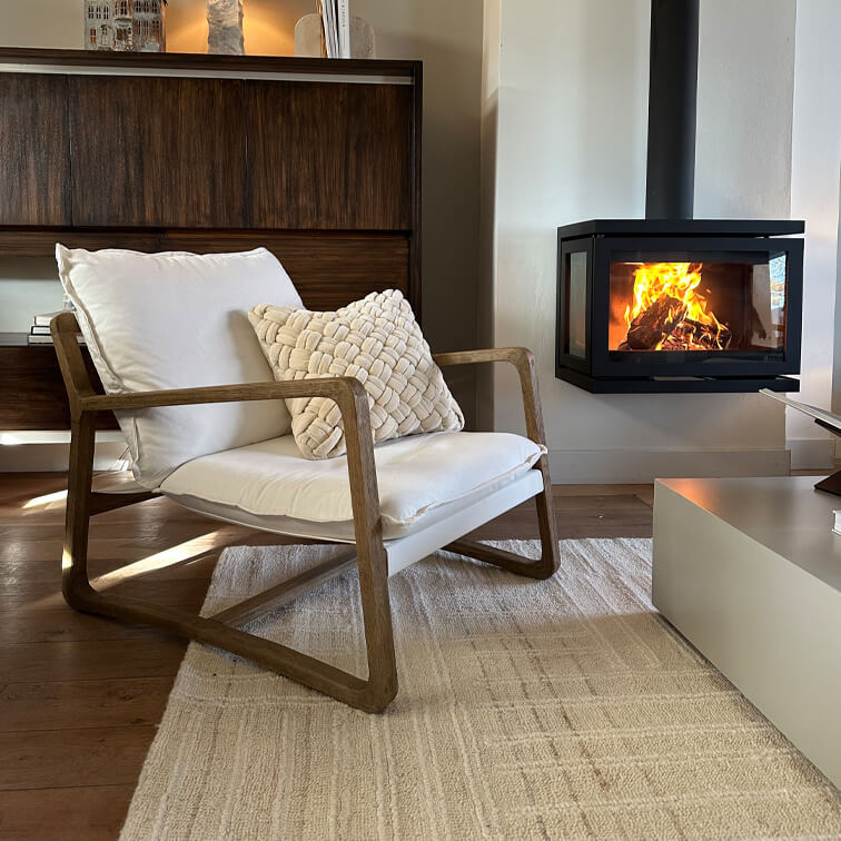 Fauteuil en bois avec coussin blanc près d'un poêle moderne dans un salon chaleureux