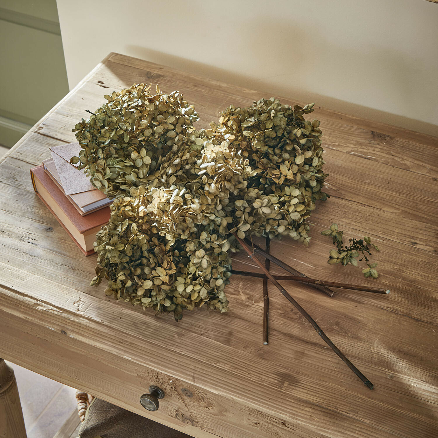 Gedroogde beige hortensia bloemen op een houten tafel met boeken en een envelop