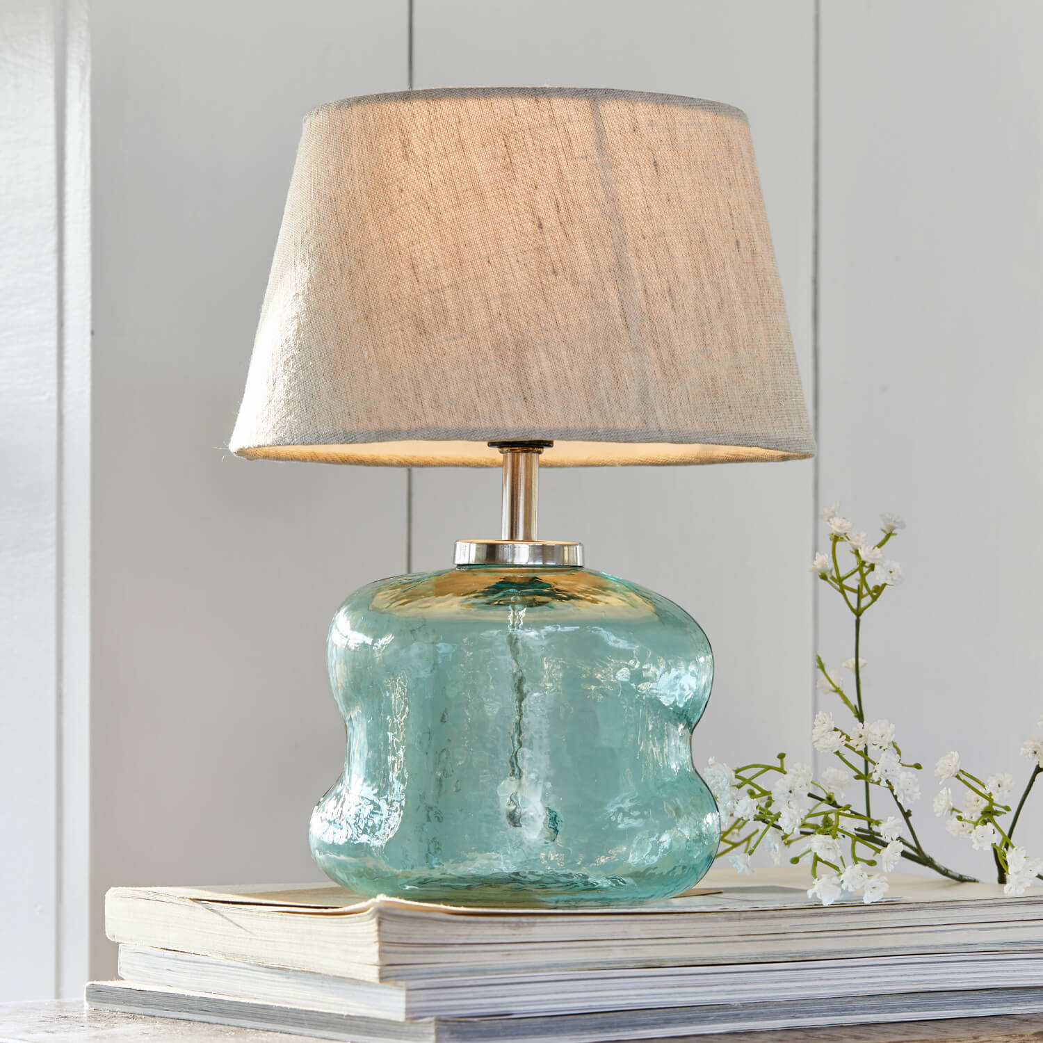 Tafellamp van blauw glas met beige kap op stapel boeken, interieurdecoratie