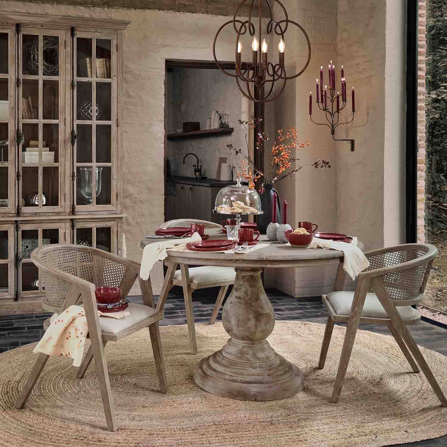 Eetkamer met ronde houten tafel en rotan stoelen in natuurlijke tinten, bordeauxrode decoraties