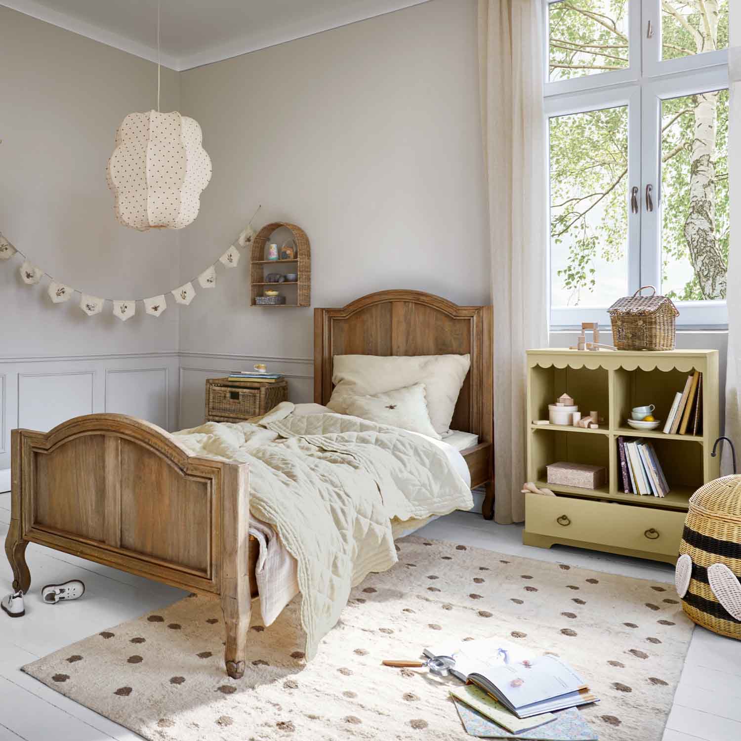 Lit enfant en bois naturel avec couette beige et petite armoire pastel pour jouets dans une chambre lumineuse
