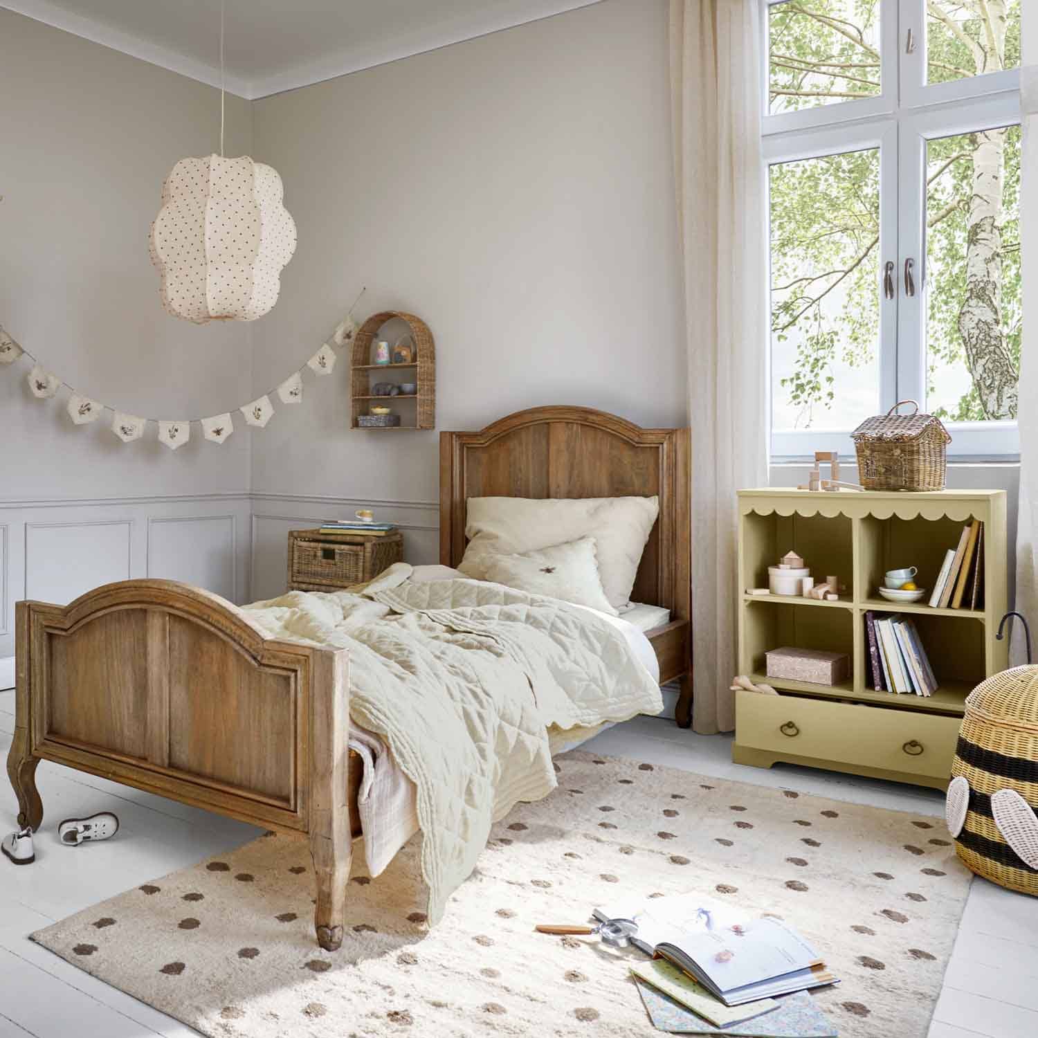 Houten kinderbed in natuurlijke kleur met beige dekbed en pastelkleurige speelgoedkast in lichte kamer