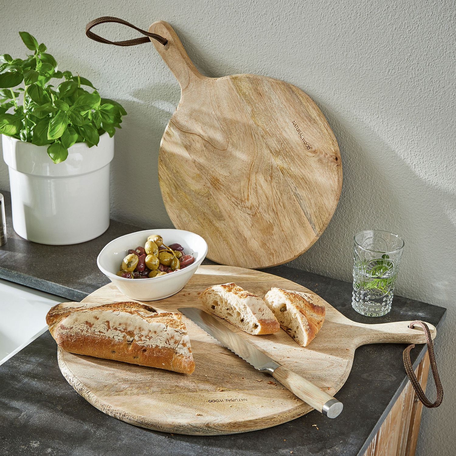 Rond snijplank van natuurlijk hout met handvat en broodmes op keukenblad