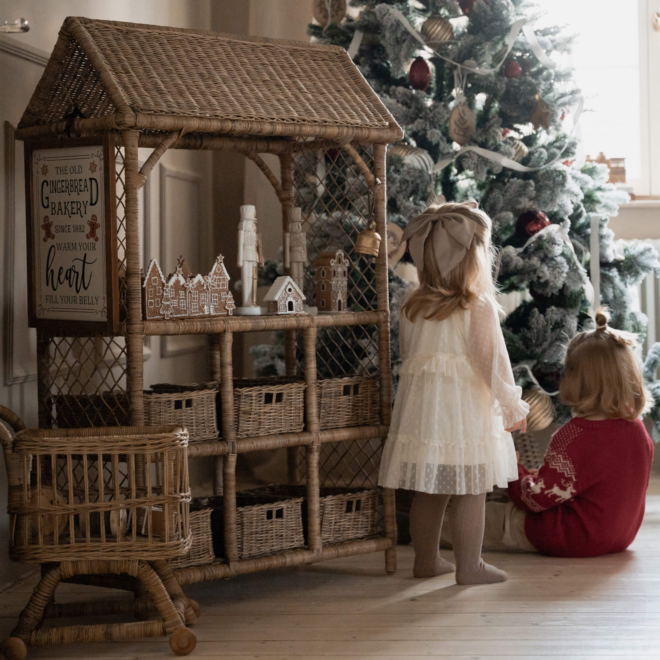 Maison en osier avec décorations en pain d'épice près d'enfants devant un sapin de Noël décoré