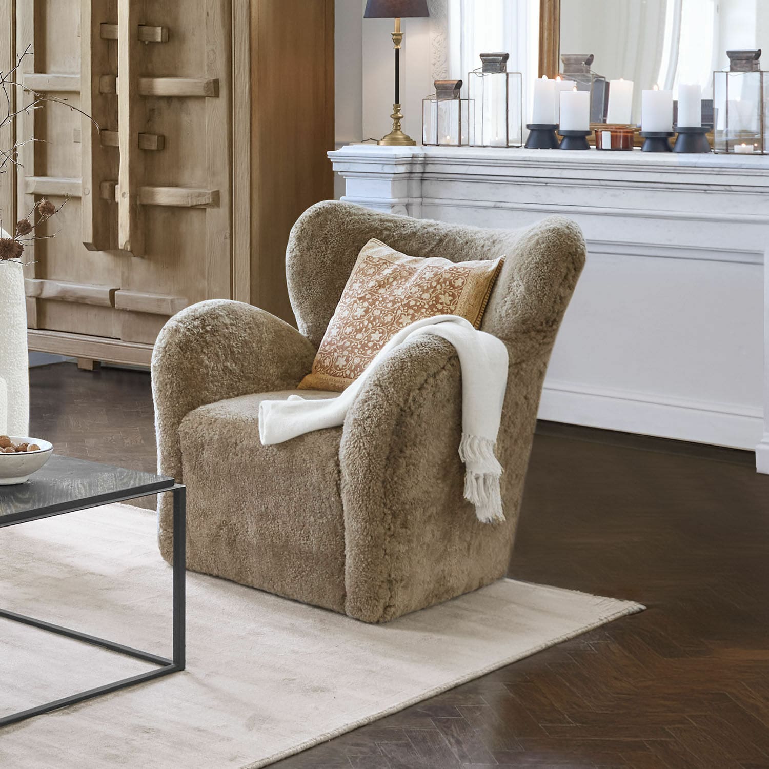 Fauteuil Ambrécourt Beige fauteuil van zachte stof met kussen en witte deken in elegante woonkamer