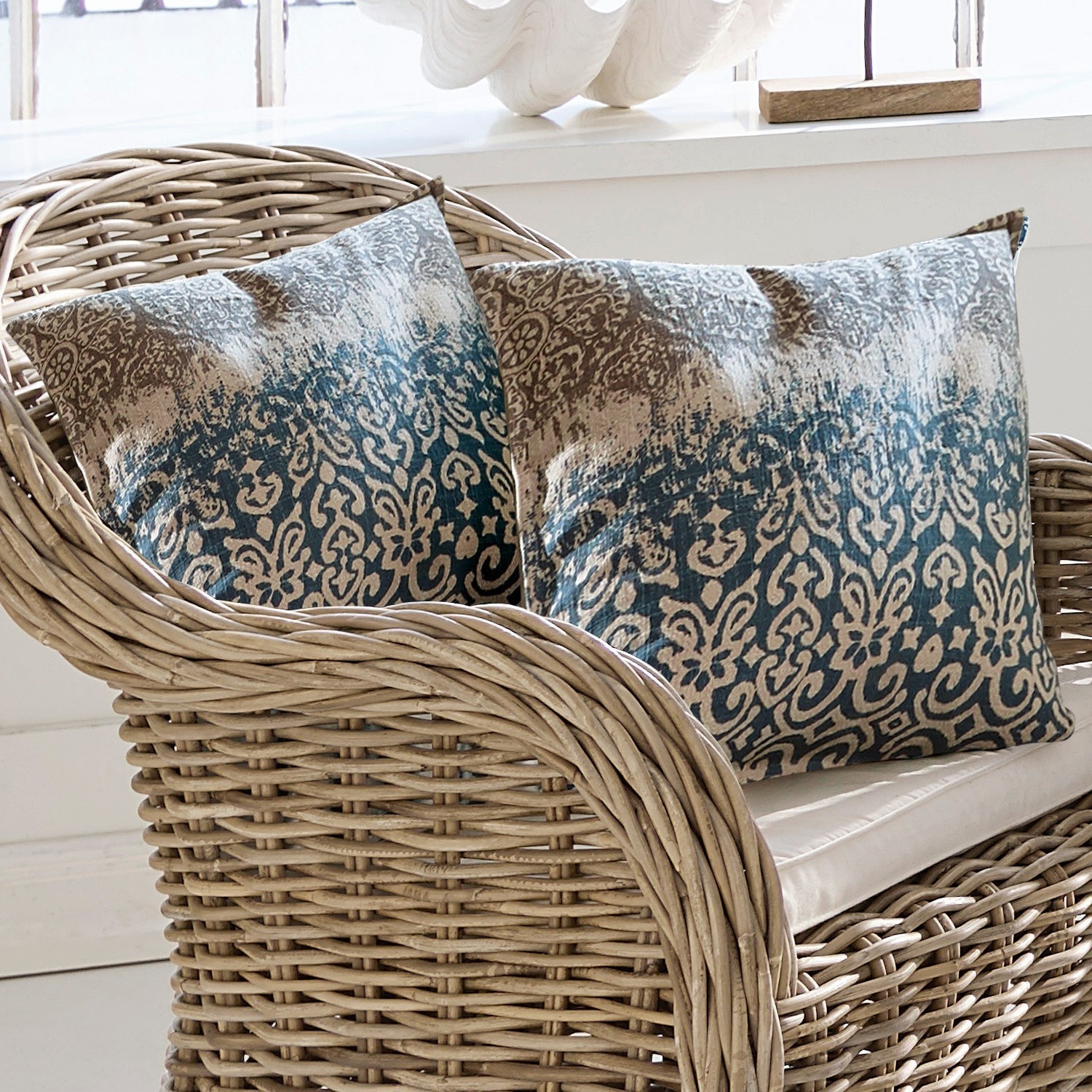 Deux coussins décoratifs à motif bleu et beige sur un fauteuil en osier naturel