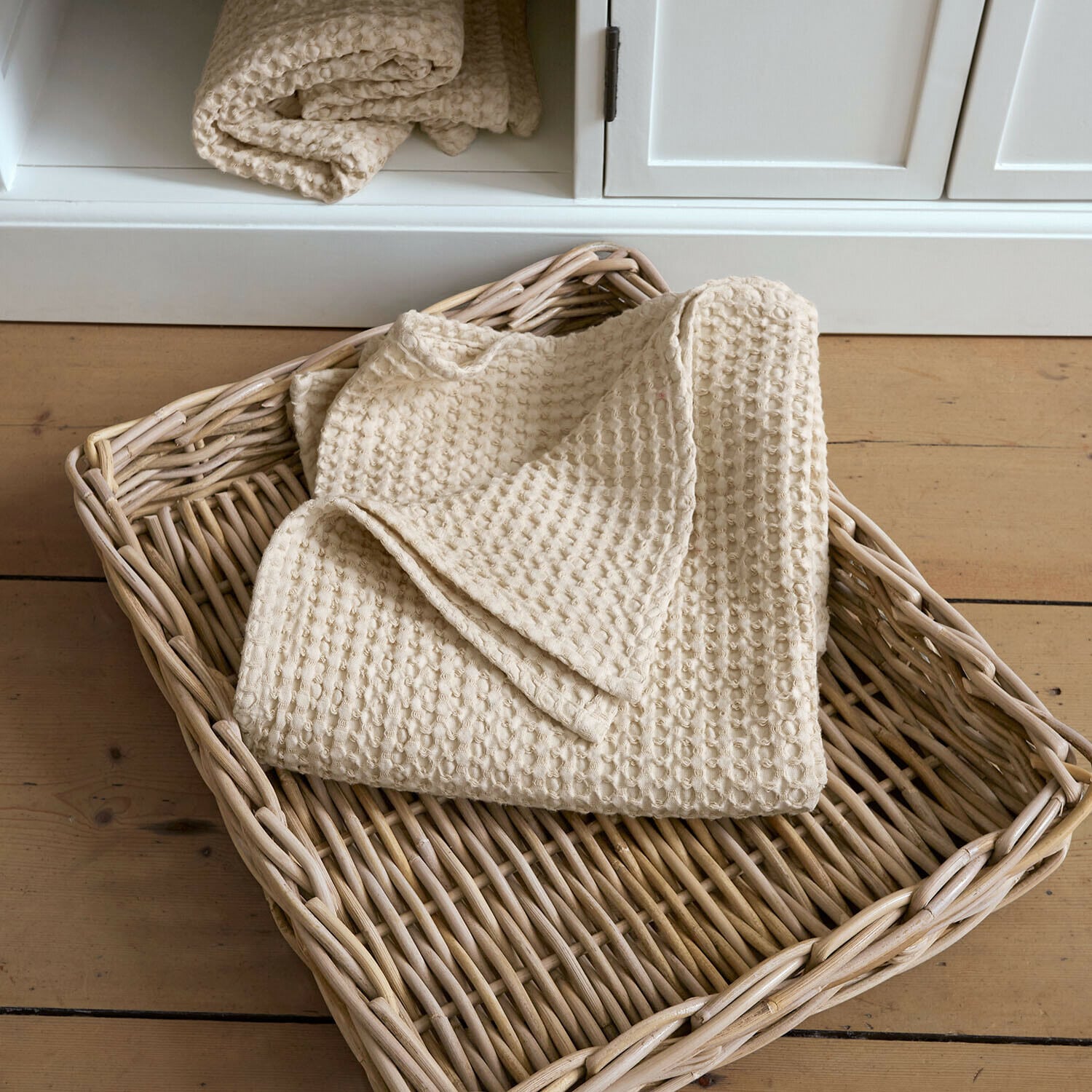 Plaid beige en coton gaufré dans un panier en osier posé sur un sol en bois clair