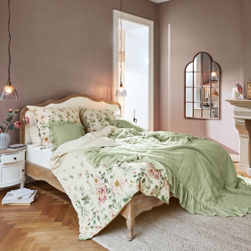 Chambre avec lit en bois, literie verte et à fleurs, lampe suspendue et miroir décoratif au mur