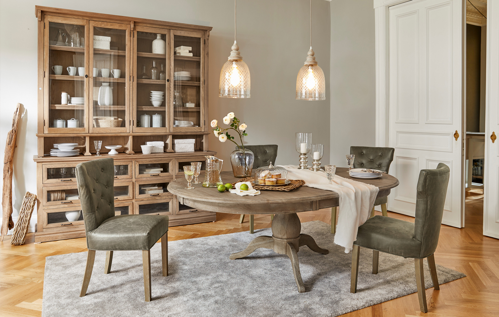 Salle à manger rustique avec table ronde en bois et chaises vertes rembourrées sur tapis gris
