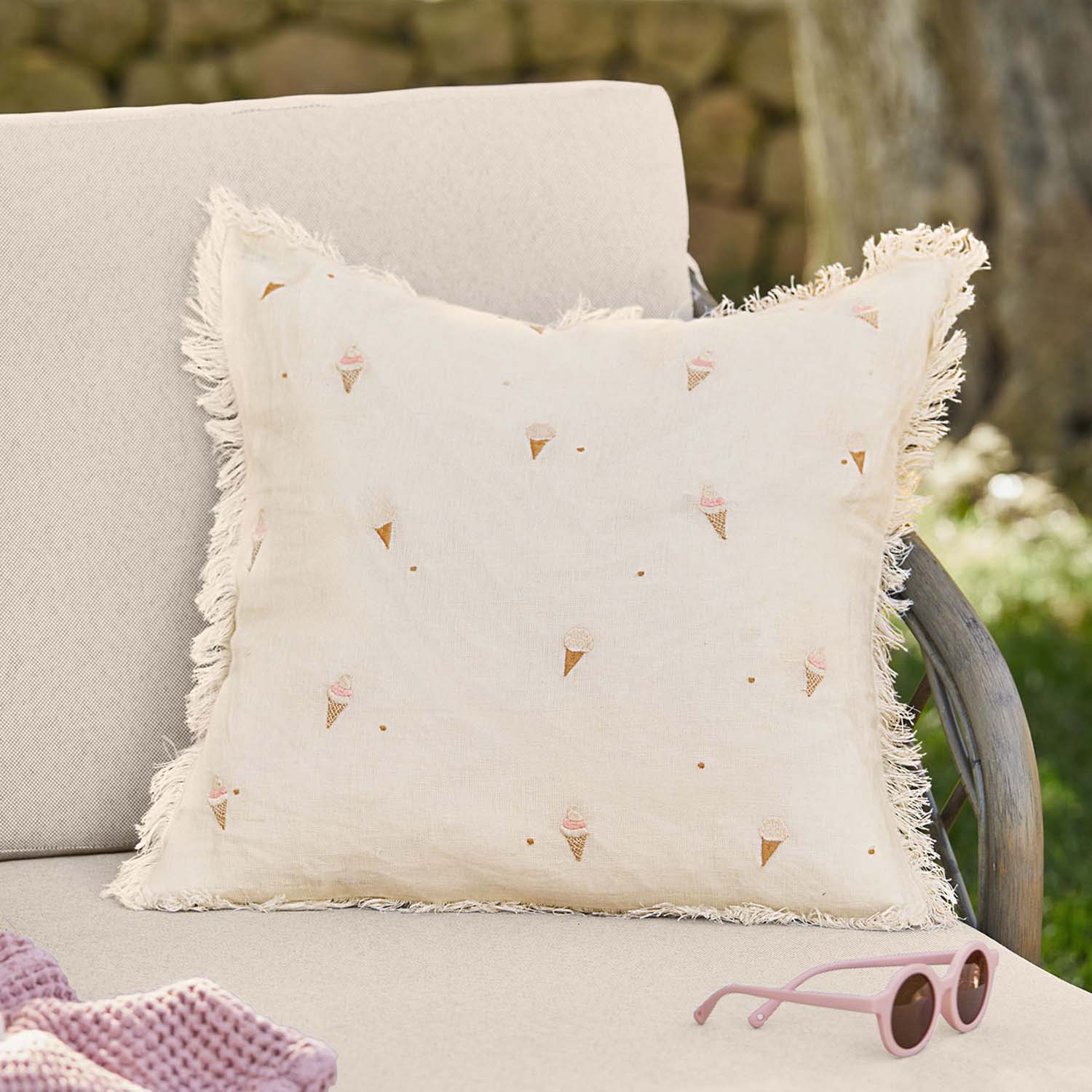 Beige linnen kussen met franjes en pastel ijsjespatroon op tuinbank