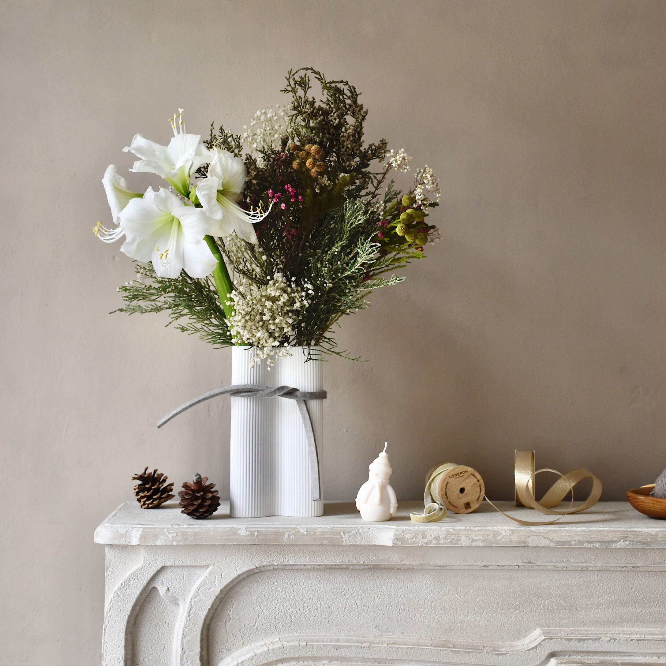Vase en céramique blanche avec fleurs blanches et feuillage vert sur une cheminée décorative blanche