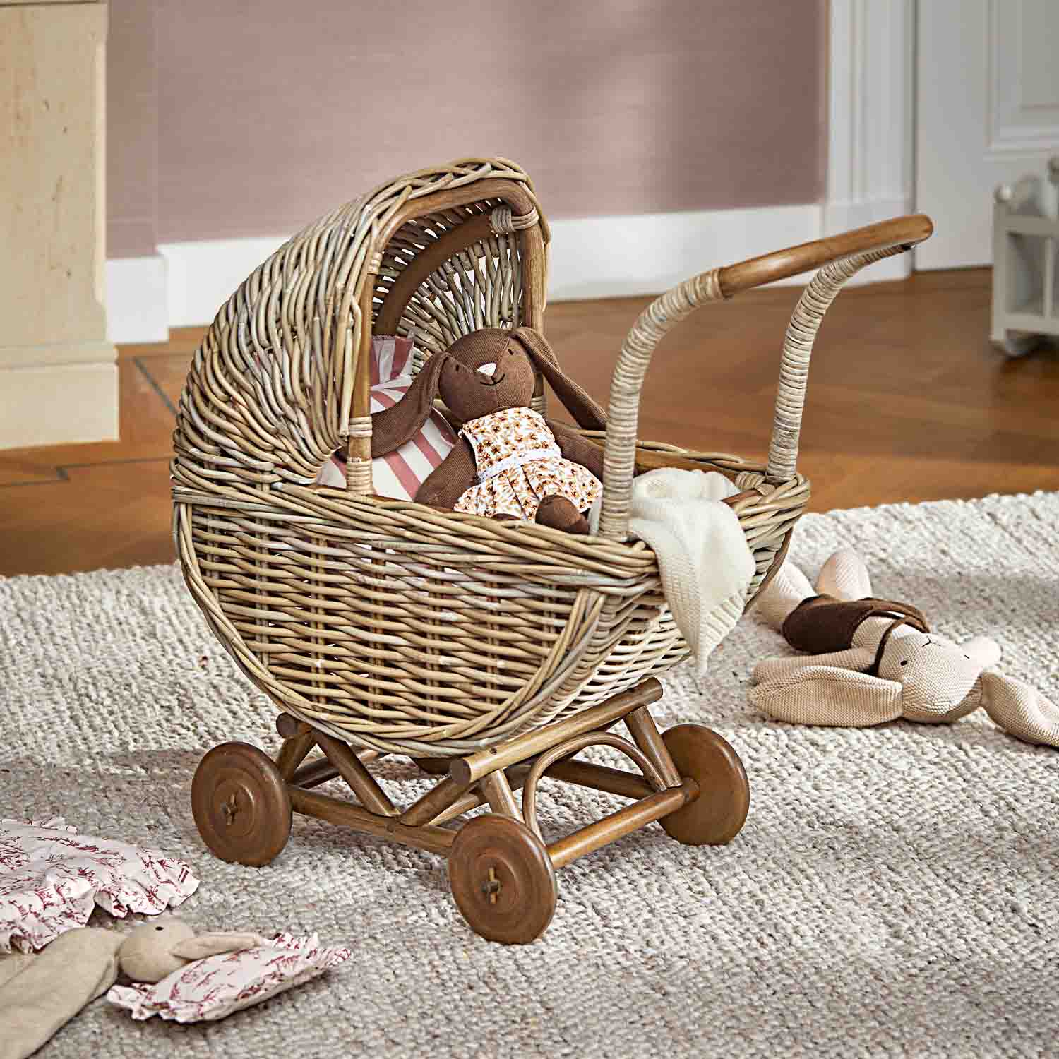 Poussette en osier avec lapin en peluche marron et couverture blanche sur tapis gris clair