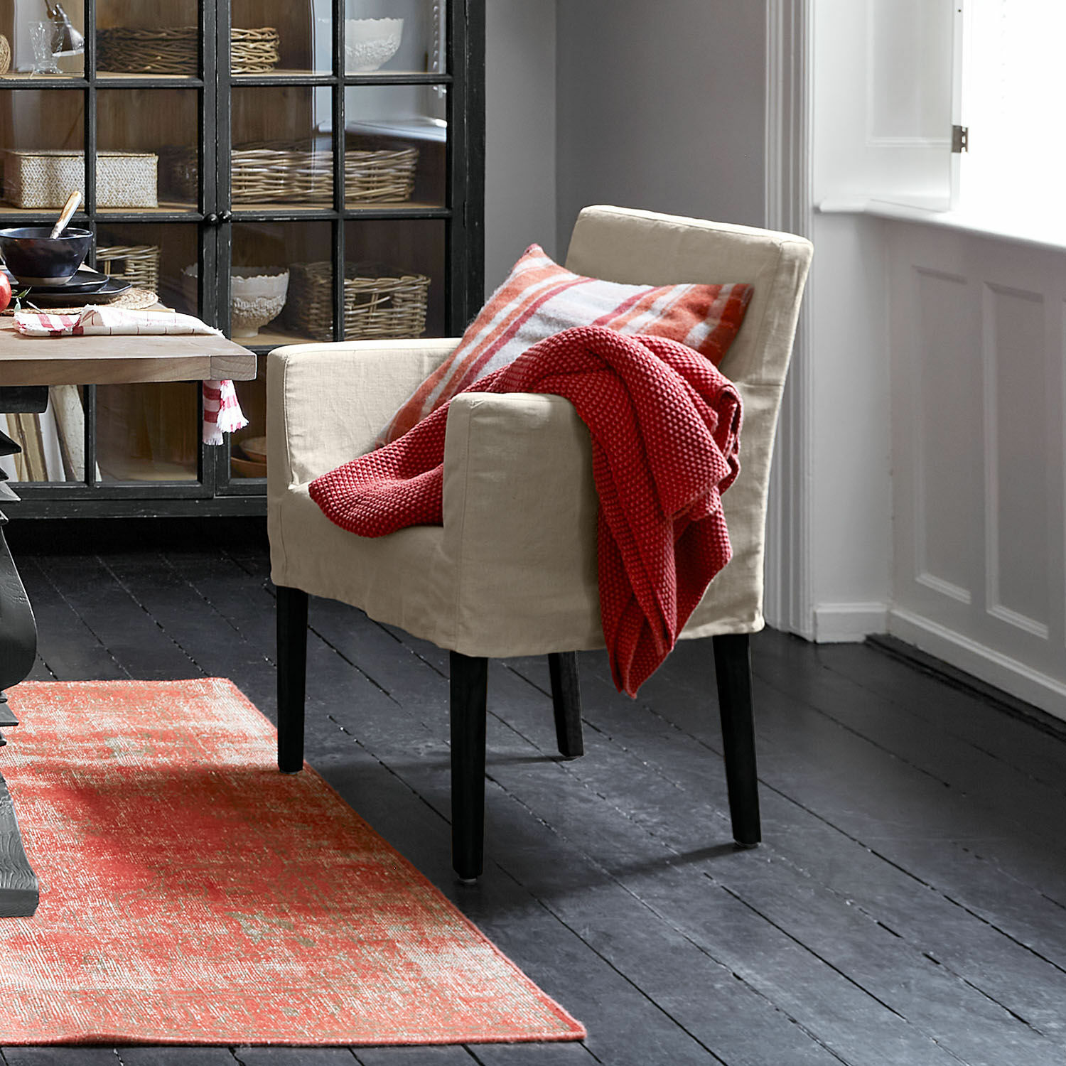 Stoel Longhill Beige stoffen fauteuil met zwarte poten, rode deken en geruit kussen, rode vloerkleed
