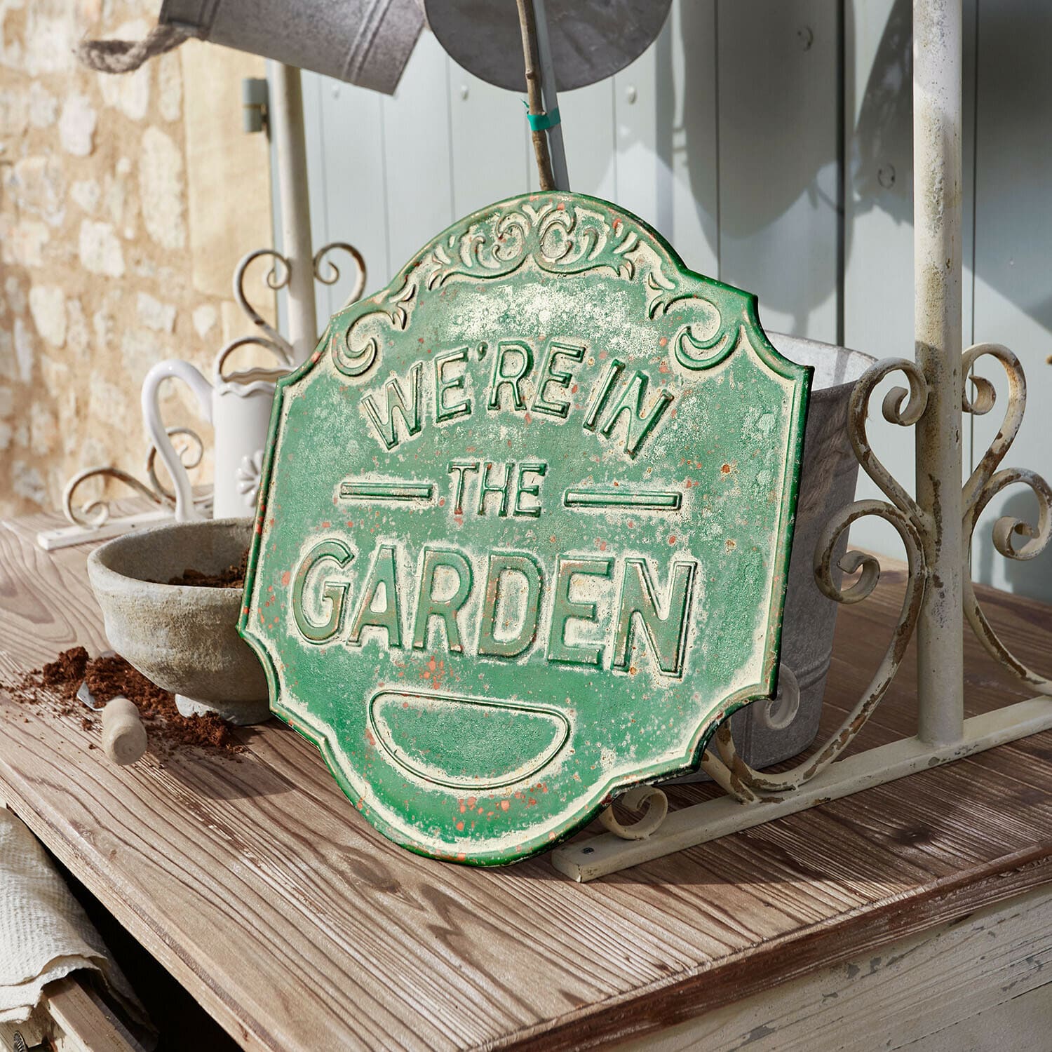 Decoratief bord Merrin Groen metalen decoratief bord met tekst We're in the Garden op houten tafel in tuin