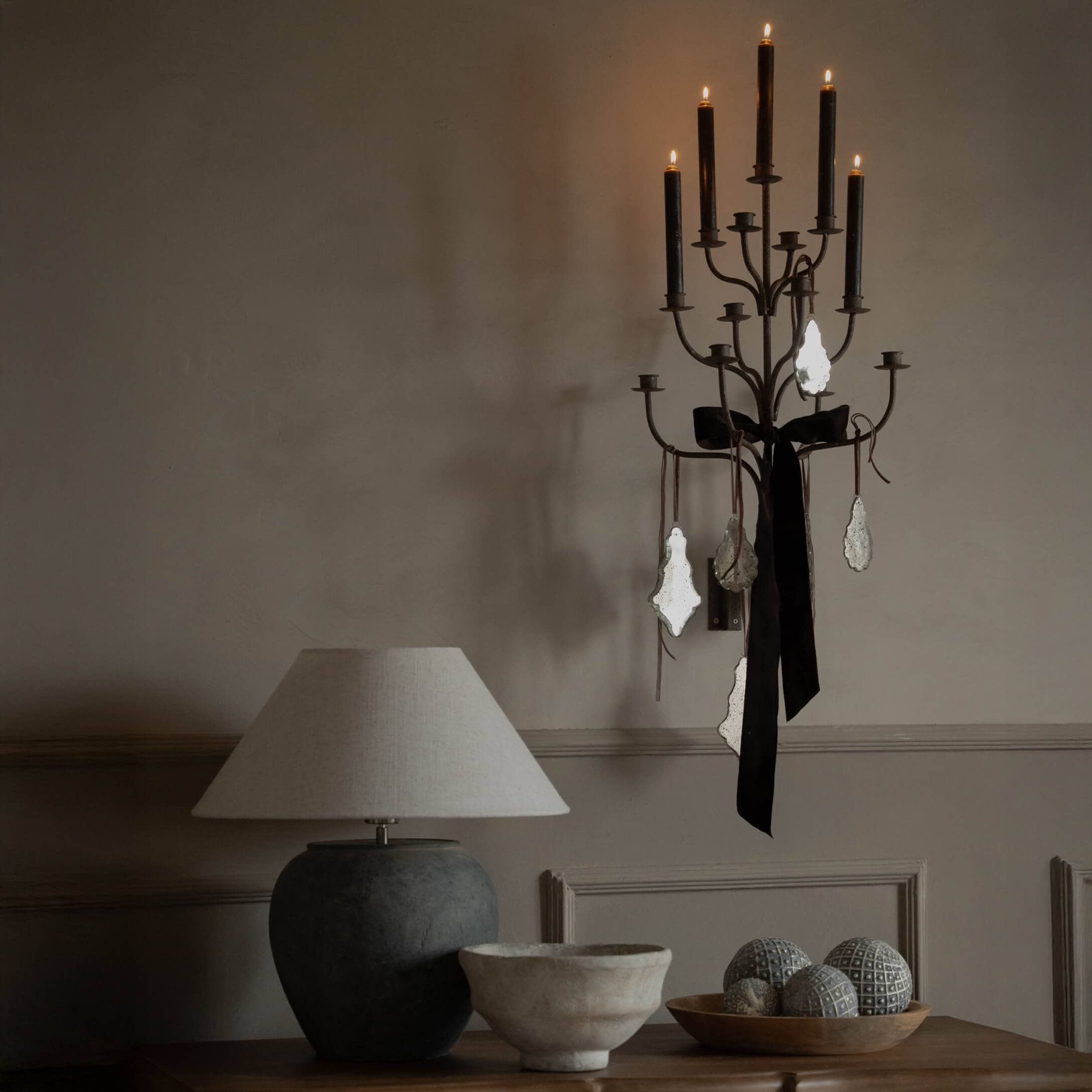 Applique murale en métal noir avec bougies noires et ruban, lampe beige sur table en bois avec décorations