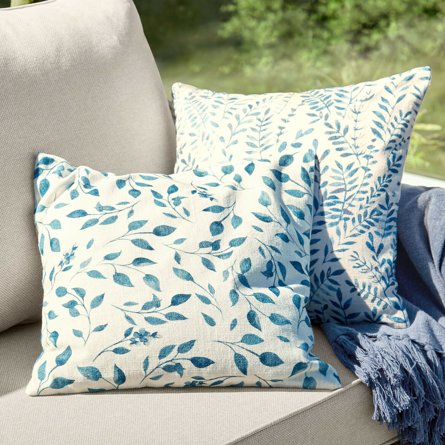 Kussenhoes set van 2 Ocevara Twee decoratieve katoenen kussens in crème met blauw bladmotief op een beige bank