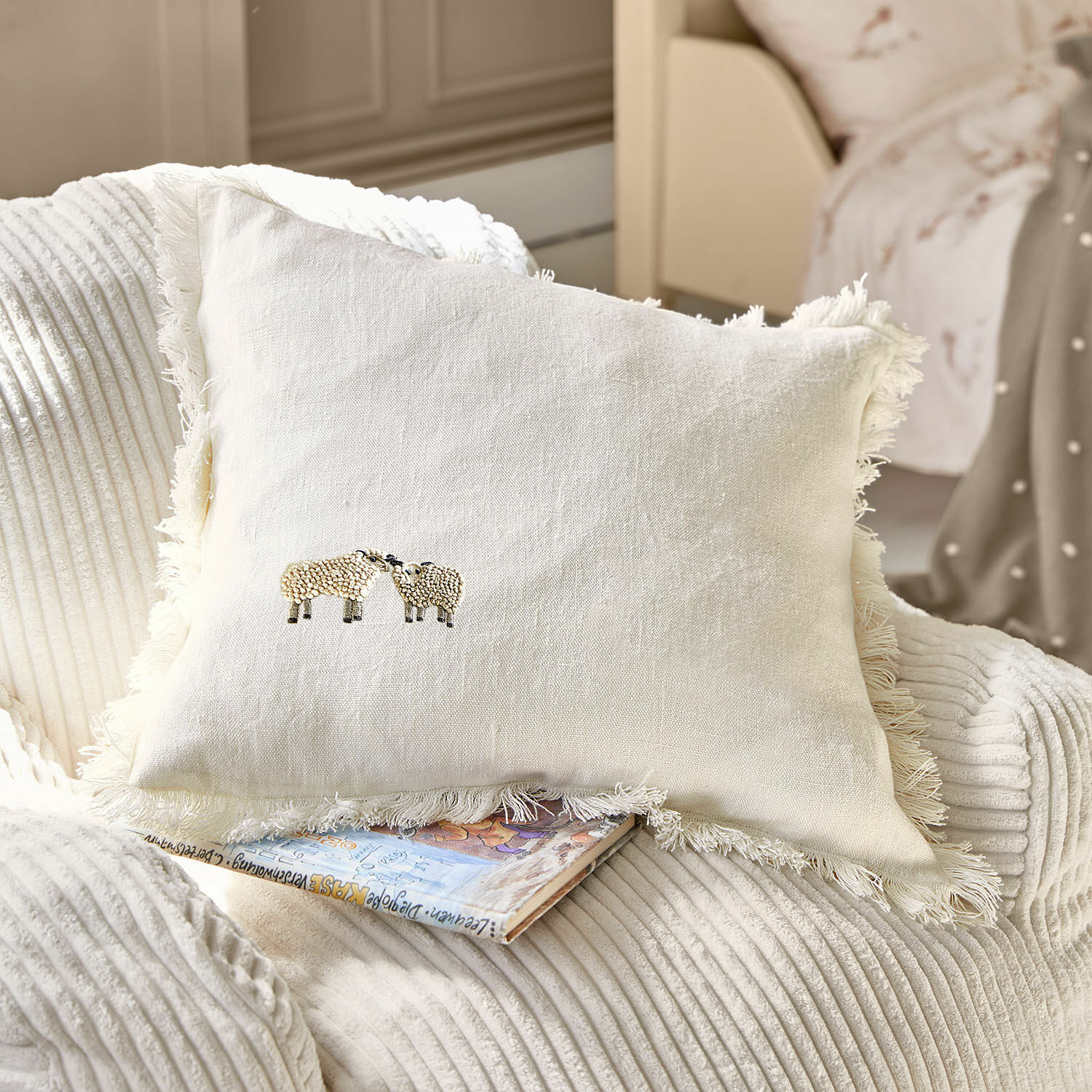 Kussenhoes Erianna Beige linnen kussen met franjes en schapenborduursel op zachte stoel, woondecoratie