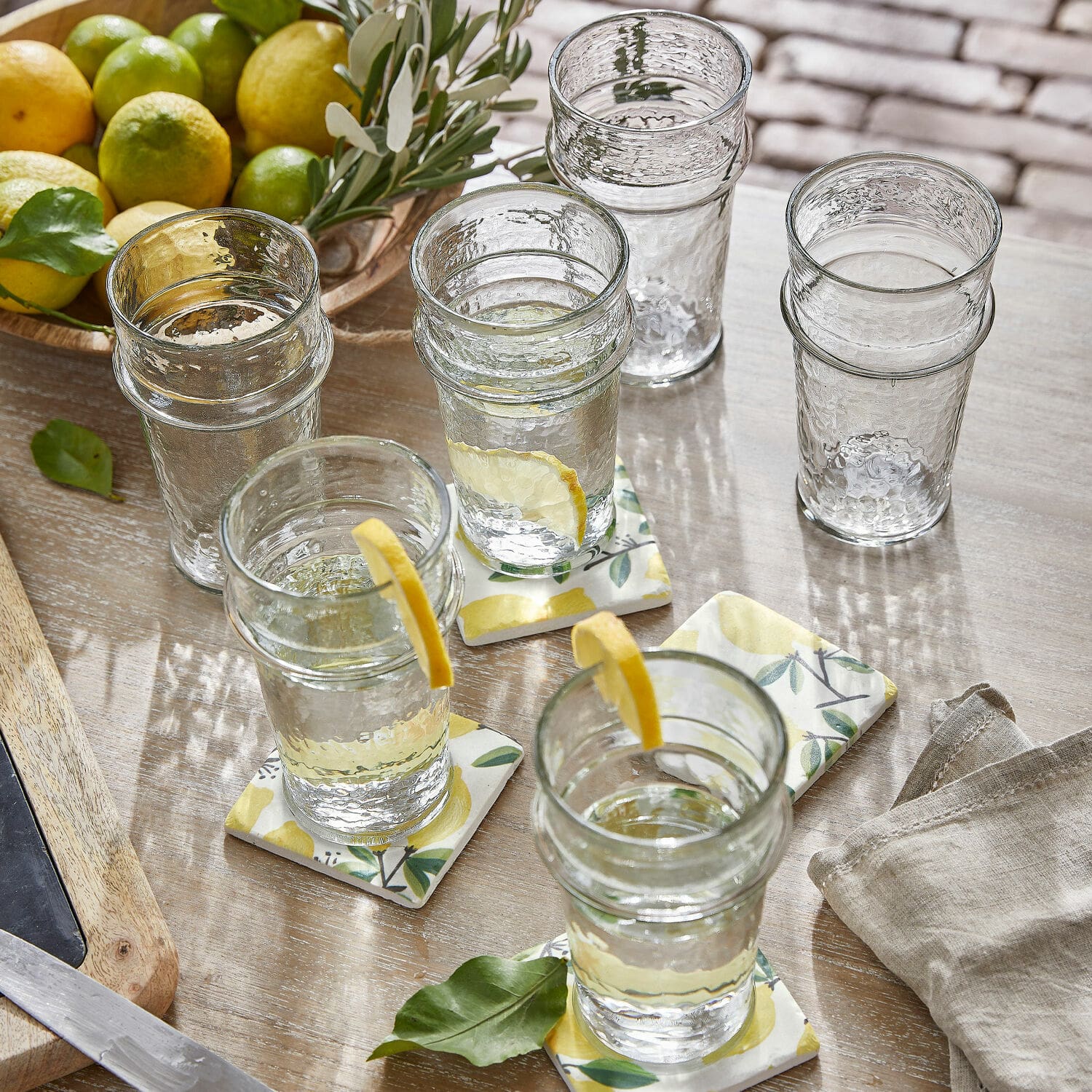 Lot de 6 verres Avrilla Verres en verre transparent texturé avec tranches de citron, sur table en bois avec agrumes à côté