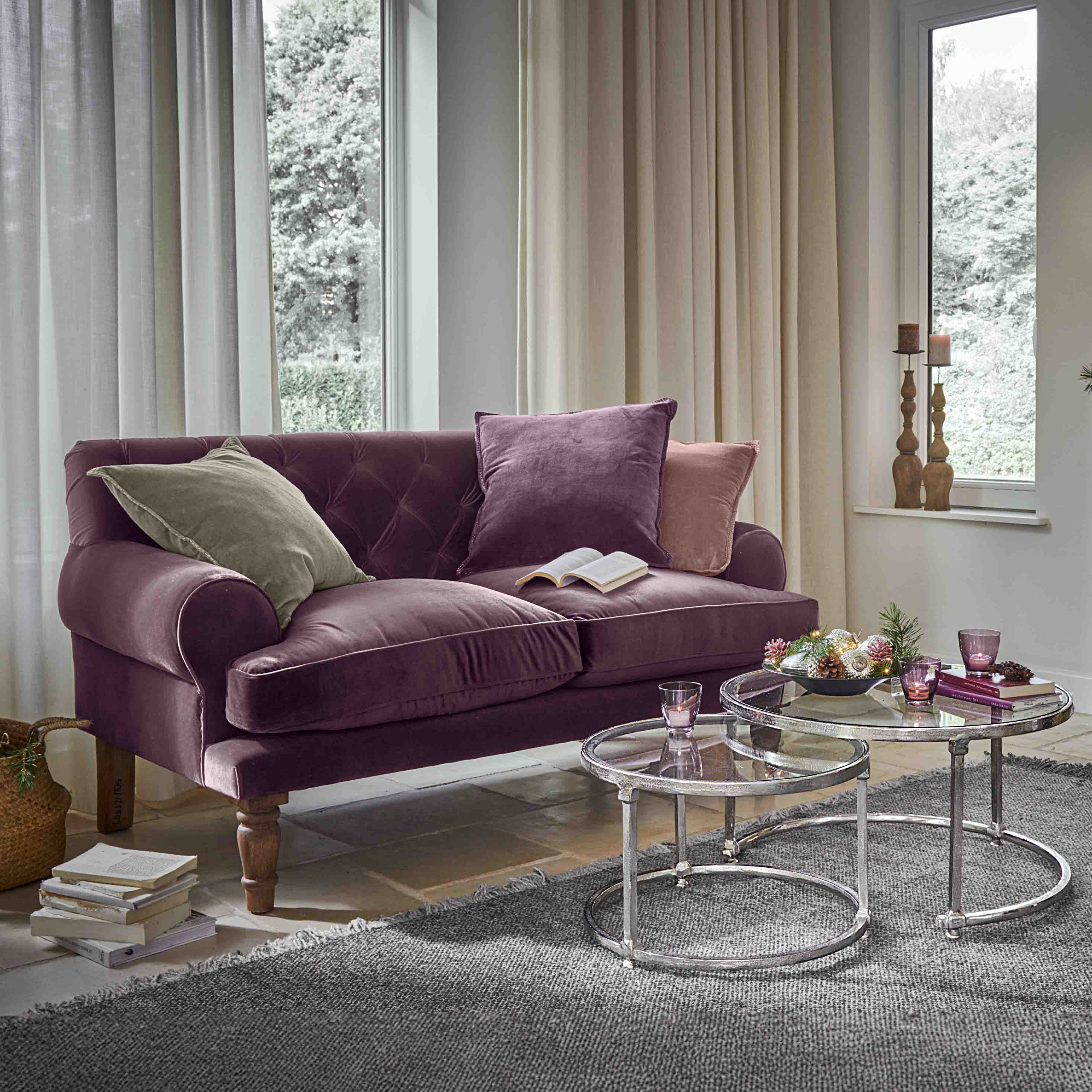 Canapé violet en velours avec coussins et tables basses en verre dans un salon lumineux