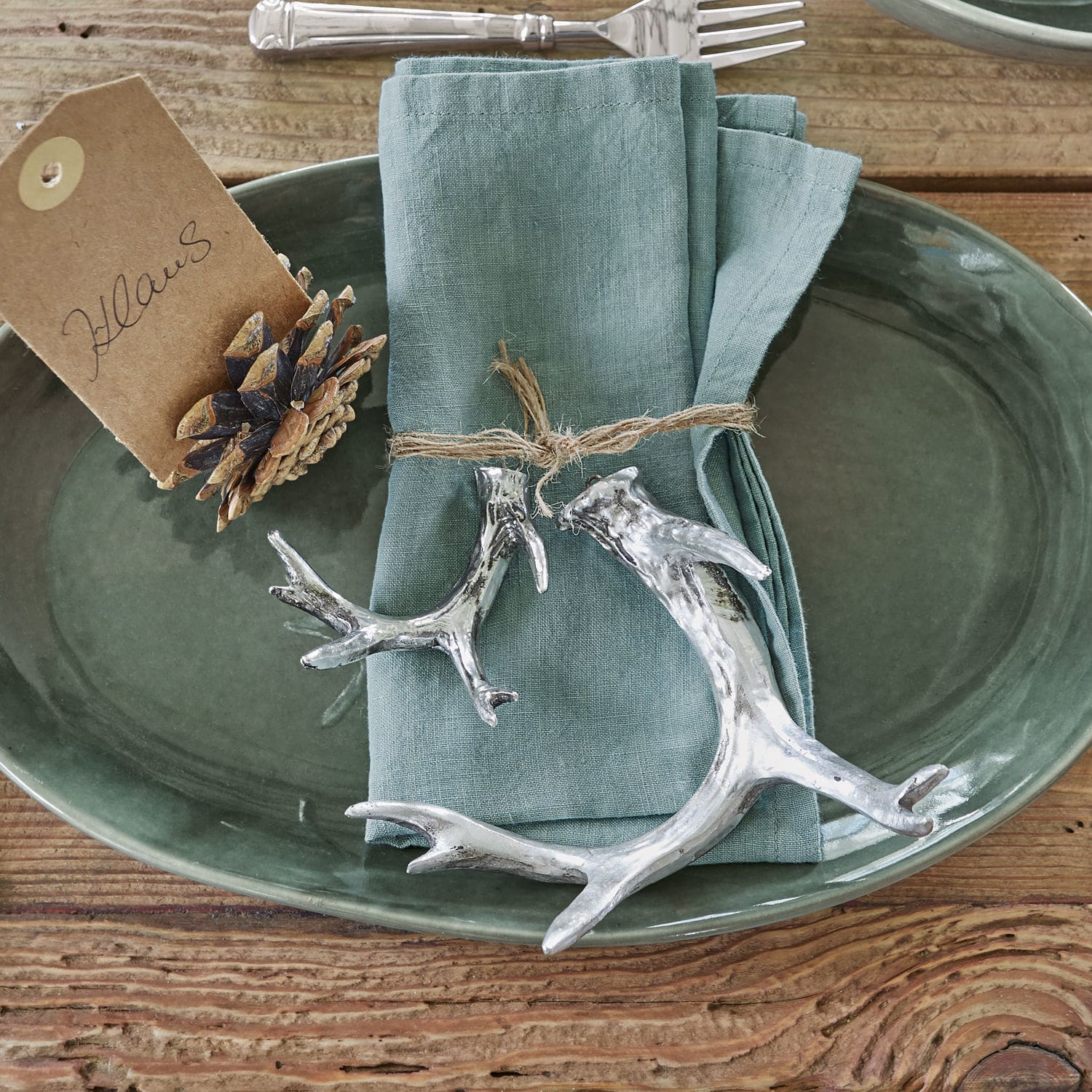 Plat en céramique verte avec serviette en lin et décorations argentées en forme de bois sur table en bois
