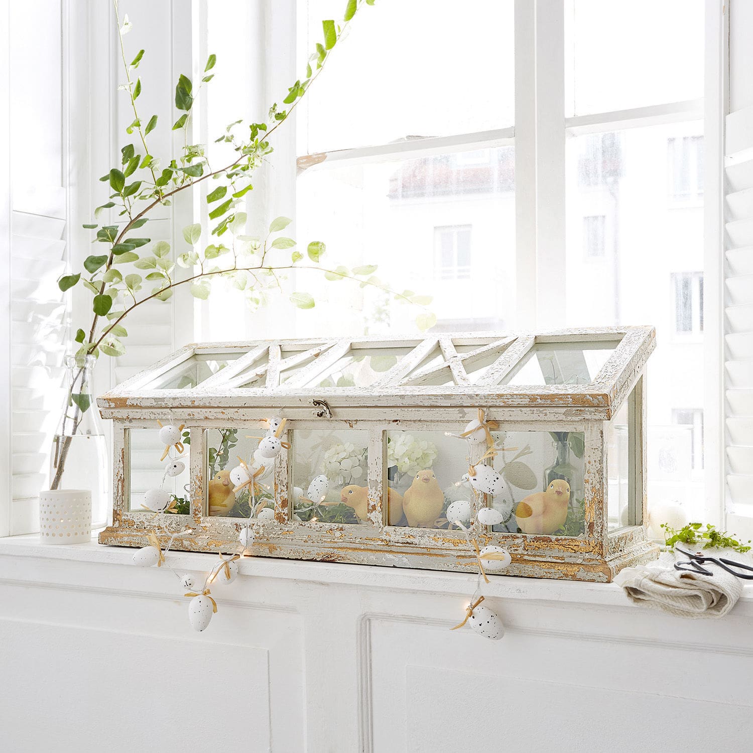 Mini serre en bois blanc vieilli avec décoration de poussins sur le rebord de la fenêtre lumineuse