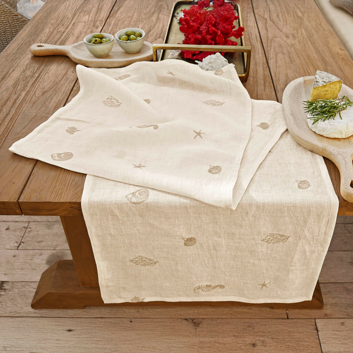 Chemin de table Celorin Chemin de table en lin beige avec motifs marins brodés sur une table en bois pour décoration intérieure