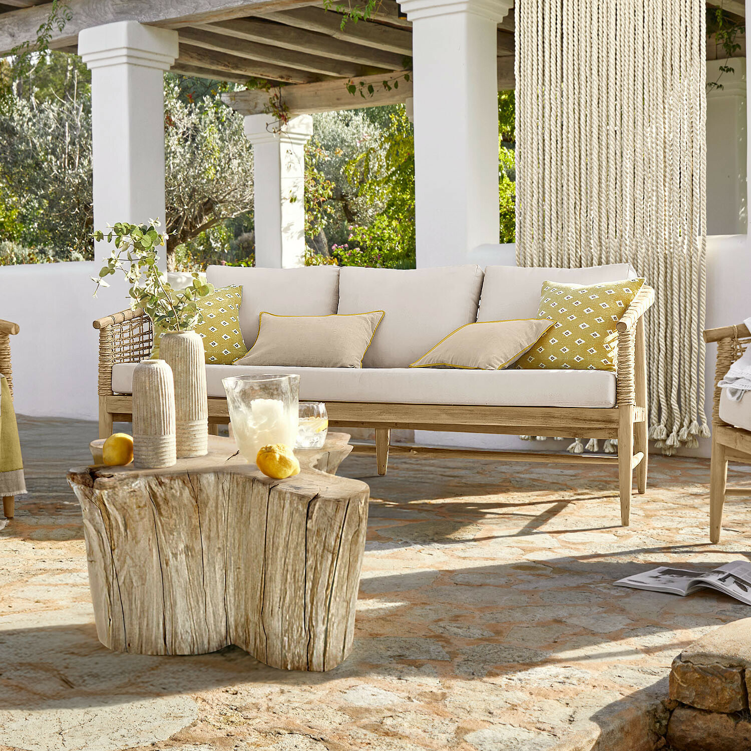 Canapé Roselva Canapé en bois clair avec coussins beige et accents jaunes sur terrasse en pierre naturelle