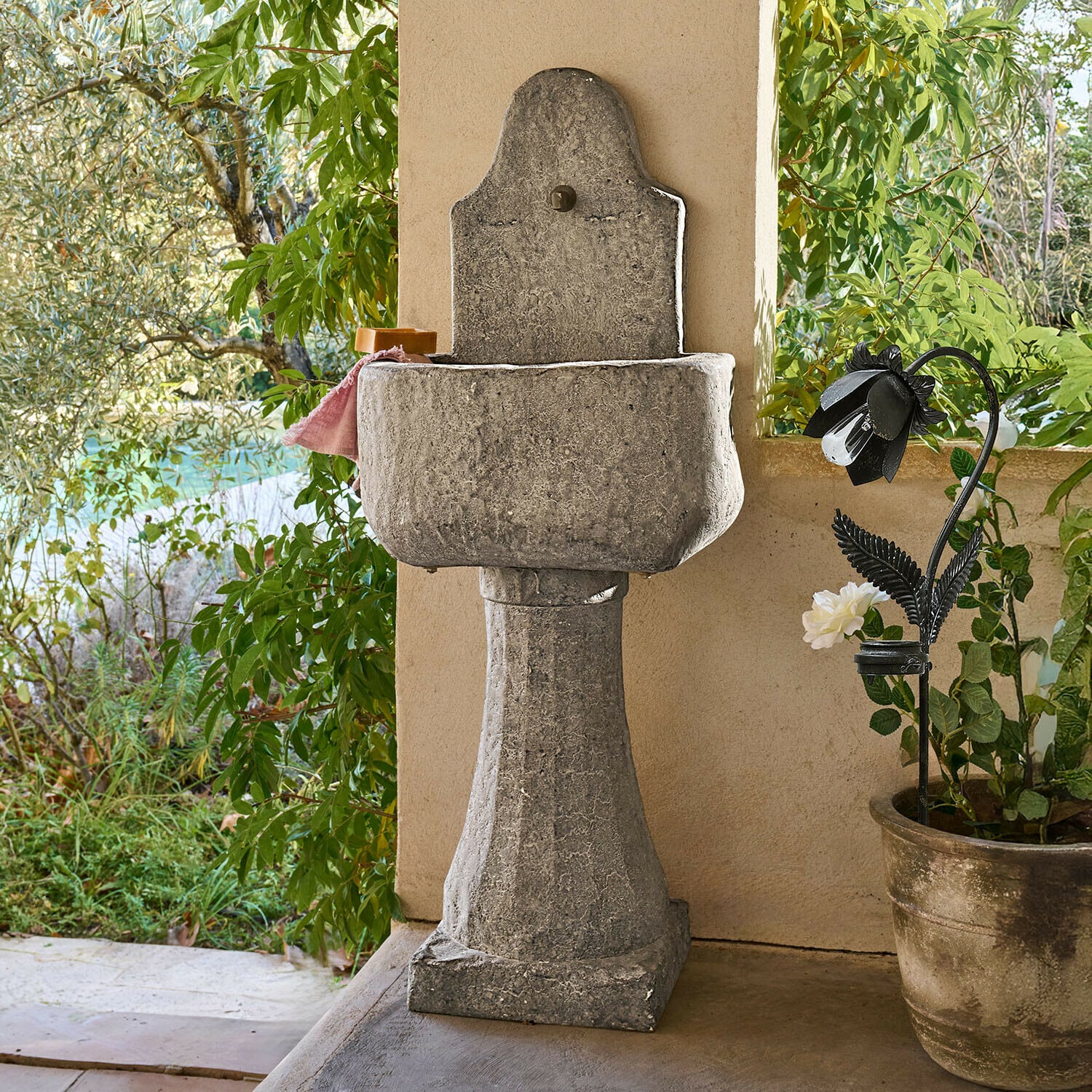 Fontaine Lurevino Lavabo de jardin en pierre grise sur colonne avec finition naturelle, entouré de plantes vertes