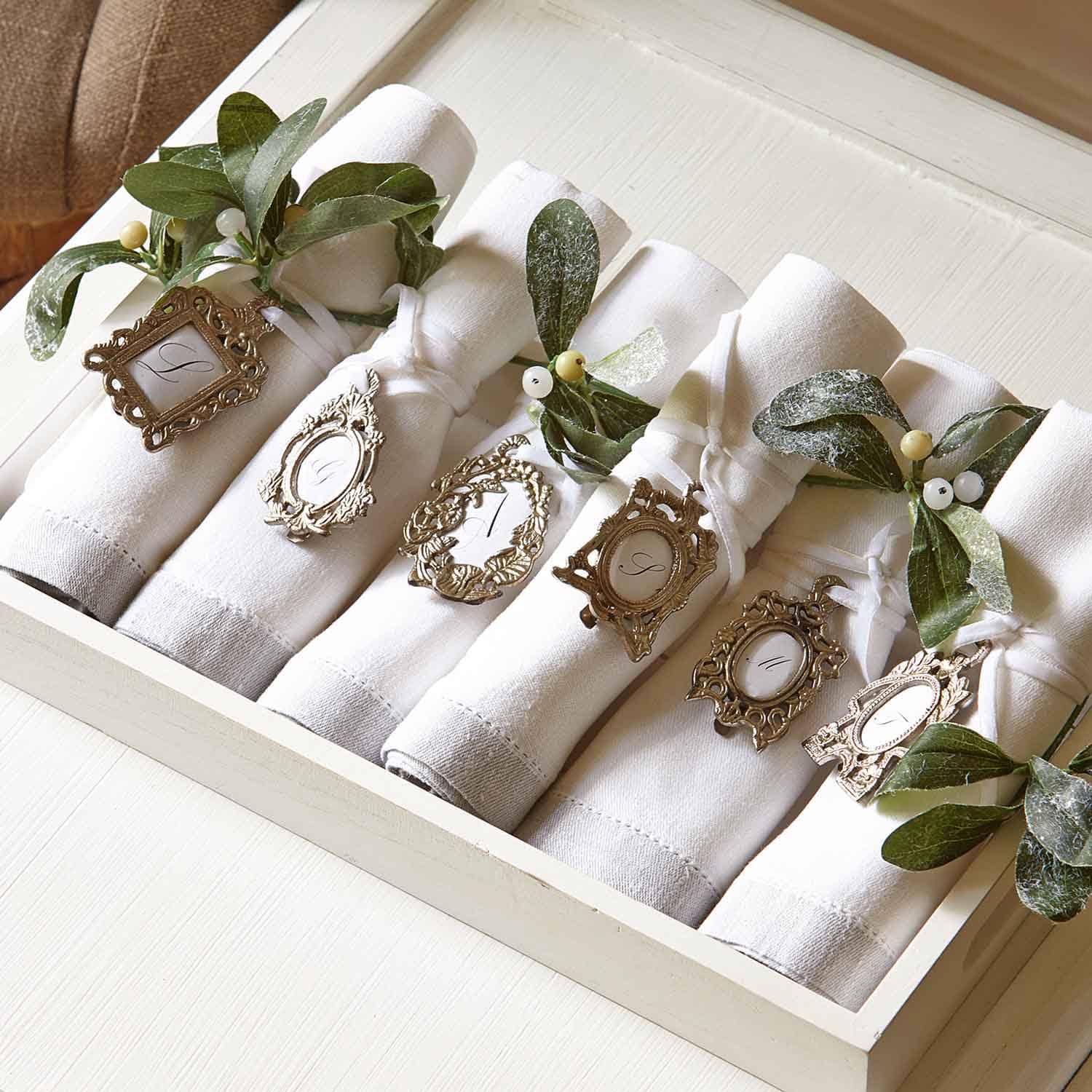 Serviettes en lin blanc avec anneaux décoratifs en métal et feuilles vertes pour table élégante.